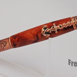 May include: A wooden pen with a copper-colored finish and nautical themed accents. The pen features an anchor, rope, and a ship's wheel design. The pen is made by Freedom On Studio.