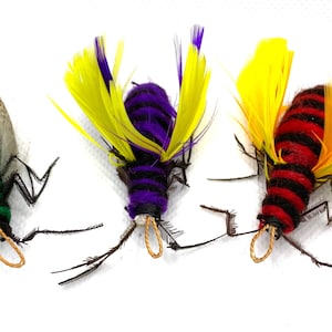 Op de afbeelding: Drie kleurrijke speelgoedinsecten met veren. De insecten zijn groen en wit, paars en geel, en rood en oranje.
