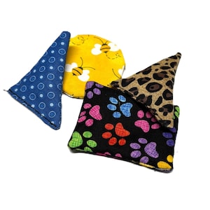 Puede incluir: Una colección de juguetes para gatos con diversas formas y patrones. Incluye un cono azul con lunares blancos, un círculo amarillo con abejas, un cuadrado negro con huellas de patas coloridas y un cono marrón con estampado de leopardo.