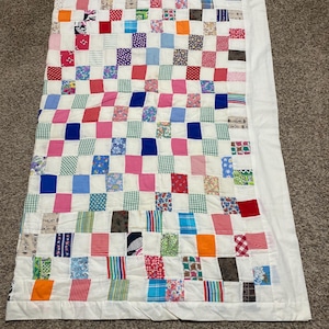May include: A patchwork quilt with a white background and squares of various colors and patterns, including pink, blue, green, red, and orange.