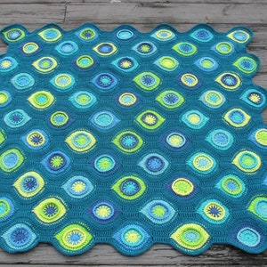 May include: A teal blue crocheted blanket with a repeating pattern of green, blue, and yellow circles. The blanket has a scalloped edge.