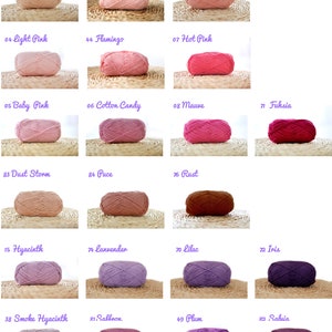 May include: A collection of yarn balls in various shades of pink, purple, and brown. The yarn balls are arranged in rows on a woven surface. The yarn balls are labelled with numbers and names, such as "Blush", "Light Sakura", "Hot Pink", "Dust Storm", "Hyacinth", "Smoke Hyacinth", "Saffron", "Plum", and "Sahvia".