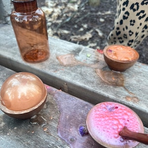 Puede incluir: Tres cuencos peque&ntilde;os llenos de l&iacute;quidos coloridos y burbujeantes. Los cuencos est&aacute;n hechos de madera y tienen un acabado natural. Los l&iacute;quidos son de color rosa, naranja y dorado met&aacute;lico. Los cuencos est&aacute;n sobre una superficie de madera.