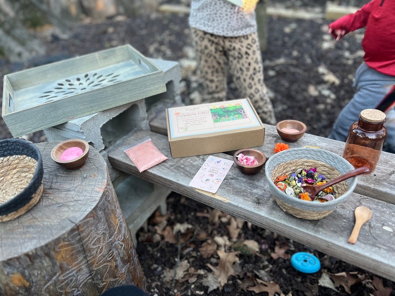 Puede incluir: Una bandeja de madera con un dise&ntilde;o tallado se encuentra sobre bloques de hormig&oacute;n. Una caja marr&oacute;n con el texto "Flower Herb" est&aacute; sobre una mesa de madera con un peque&ntilde;o cuenco de polvo rosa, un peque&ntilde;o cuenco de flores secas, un cuenco m&aacute;s grande de flores y hierbas secas, una peque&ntilde;a cuchara y una botella de vidrio con un tap&oacute;n de corcho.