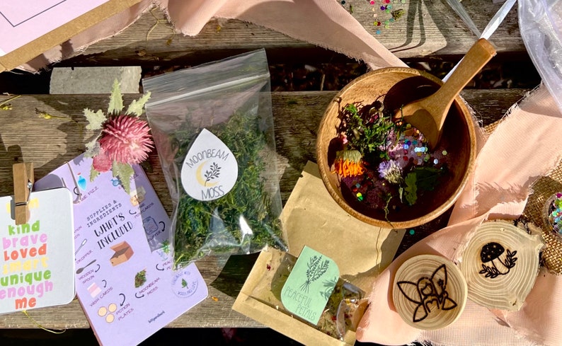 May include: A craft kit with a variety of items, including dried moss, flower petals, glitter, and wooden decorations. The kit also includes a booklet with instructions and a list of supplies. The text on the booklet reads "Supplies & Ingredients What's Included".