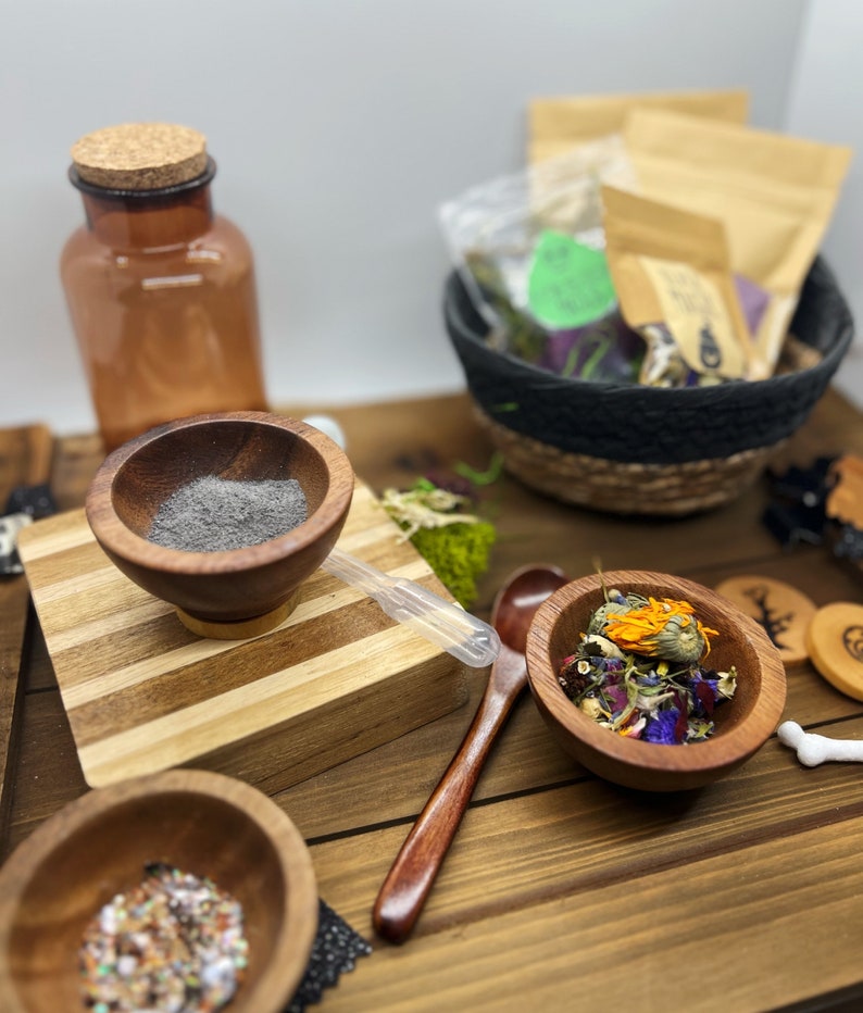K&ouml;nnte beinhalten: Ein Holztisch zeigt Apothekenartikel. Kleine Holzschalen enthalten Kr&auml;uter, Pulver und getrocknete Blumen. Eine braune Glasflasche mit Korken und ein geflochtener Korb mit Papiert&uuml;ten sind ebenfalls vorhanden.