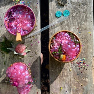 May include: Three bowls filled with pink iridescent slime with glitter and small flowers on a wooden surface.