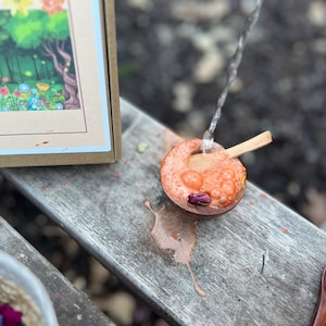 Puede incluir: Un peque&ntilde;o cuenco de madera lleno de un l&iacute;quido rosa y burbujas. Se est&aacute; vertiendo agua en el cuenco desde arriba. Una cuchara de madera descansa en el borde del cuenco.