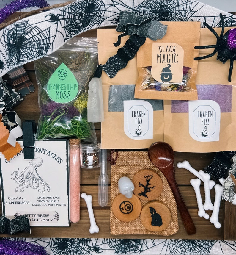 K&ouml;nnte beinhalten: Eine Sammlung von Halloween-Artikeln, darunter Beutel mit der Aufschrift "Black Magic" und "Fraken Fizz", ein Beutel mit "Monster Moss", Untersetzer aus Holz, ein Holzl&ouml;ffel und knochenf&ouml;rmige Dekorationen. Die Artikel sind auf einer Holzoberfl&auml;che angeordnet.