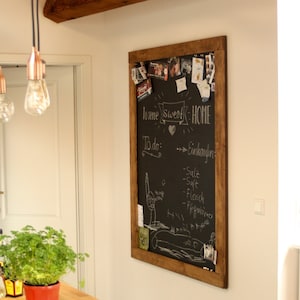 May include: A wooden framed chalkboard with the words "home sweet home" written in white chalk. The chalkboard is decorated with photos, notes, and other items. The chalkboard is hanging on a white wall in a kitchen.