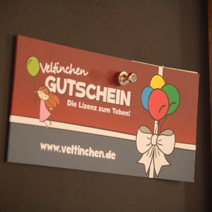 May include: A red and gray gift certificate with the text "Veltinchen Gutschein" and "Die Lizenz zum Toben!"  The certificate features a cartoon girl holding a balloon and a bow with balloons.