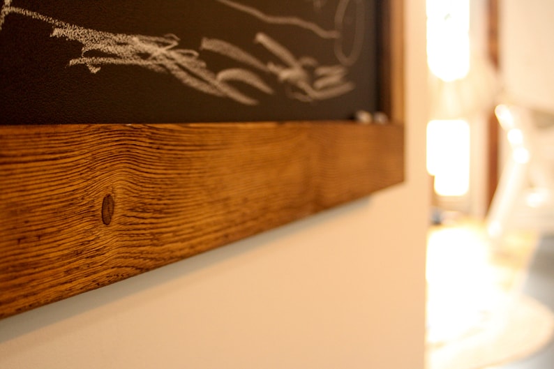 May include: A close-up of a wooden frame with a dark brown stain. The frame is made of reclaimed wood with a knot in the center. The frame is mounted on a white wall.
