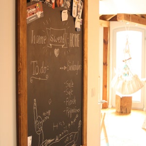 May include: A wooden framed chalkboard with the words "home sweet home" written in white chalk. The chalkboard also has a list of items to buy written in white chalk, including "salt", "juice", "meat", and "pepperoni".