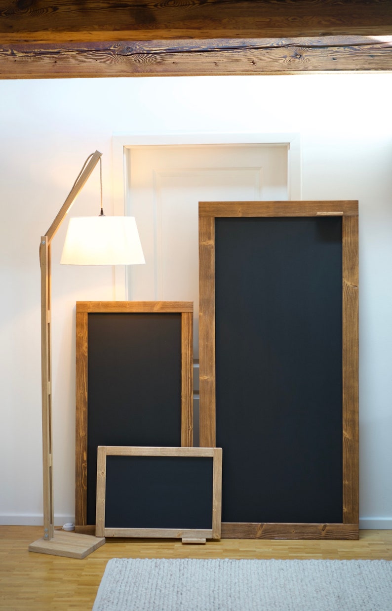 May include: Three wooden framed blackboards of different sizes, with the largest one standing upright and the two smaller ones lying flat on the floor. The boards are all black and have a rustic wooden frame.
