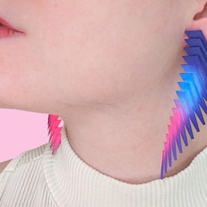 May include: A pair of geometric earrings with a gradient of pink, blue, and purple. The earrings are made of multiple layers of thin, triangular shapes.