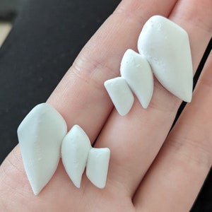 May include: Two pairs of white, 3D printed, geometric shaped earrings. The earrings are made of a smooth, matte white plastic.