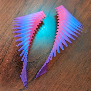 May include: Two pairs of colorful, layered, geometric shapes made of plastic. The shapes are a gradient of pink and blue.