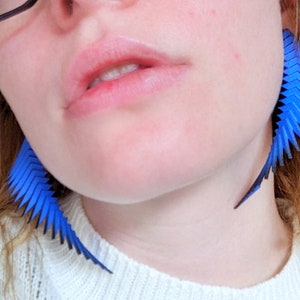 May include: A pair of blue geometric earrings with a sharp, angular design. The earrings are made of a lightweight material and have a modern, edgy look.
