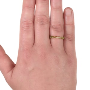May include: A gold band ring with small, round, yellow gemstones set in a continuous line.