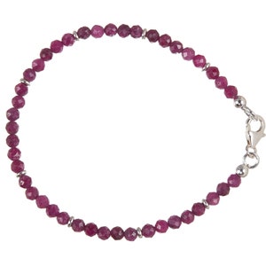 Könnte beinhalten: Ein filigranes Armband mit facettierten, tiefroten Rubinperlen. Die Perlen sind mit kleinen silberfarbenen Abstandshaltern und einem silbernen Verschluss aufgereiht. Das Armband ist für das Handgelenk konzipiert.