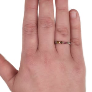 May include: A ring with a band of small, colourful gemstones. The ring is on a person's finger.