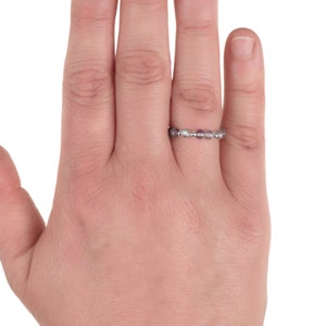 May include: A delicate ring with small, round, iridescent beads strung together. The beads have a subtle colour variation, ranging from clear to pale purple. The ring is worn on a finger, showcasing its minimalist design and elegant simplicity.