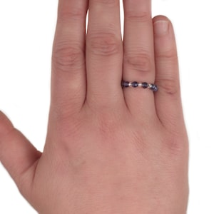 May include: A ring made of small, round, purple beads with silver accents. The ring is worn on the middle finger of a hand.