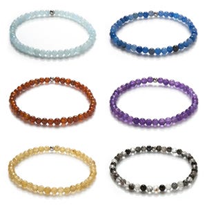 Könnte beinhalten: Sechs Perlenarmbänder in verschiedenen Farben, darunter hellblau, dunkelblau, braun, lila, hellgelb und grau. Jedes Armband hat einen silbernen Verschluss.
