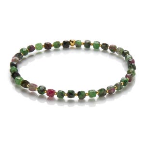 Op de afbeelding: Een delicate armband gemaakt van kleine, vierkante groene, roze en zwarte edelstenen. De armband is geregen op een gouden ketting.