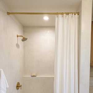 May include: A modern bathroom featuring a white bathtub, shower curtain, and walls. The shower fixtures and curtain rail are gold. A white towel hangs on the wall. A bar of soap sits on a shelf above the tub.