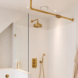 May include: A brass shower system featuring a ceiling-mounted curtain rod, a round rainfall shower head, a handheld shower wand with a flexible hose, and a triple-handle control valve, all set against white rectangular wall tiles.
