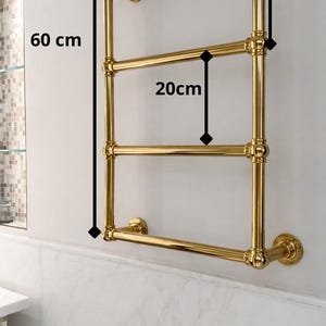 May include: A gold-colored towel rack, 23.6 inches tall and 13.8 inches wide, with three horizontal bars. The bars are spaced 7.9 inches apart. The rack is mounted on a white wall above a marble-tiled surface.