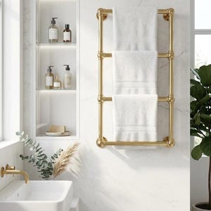 May include: A gold-colored towel rack with three white towels hanging on it. The rack is mounted on a white marble wall in a bathroom setting. The bathroom also features a white sink, a built-in shelf with toiletries, and a potted plant.