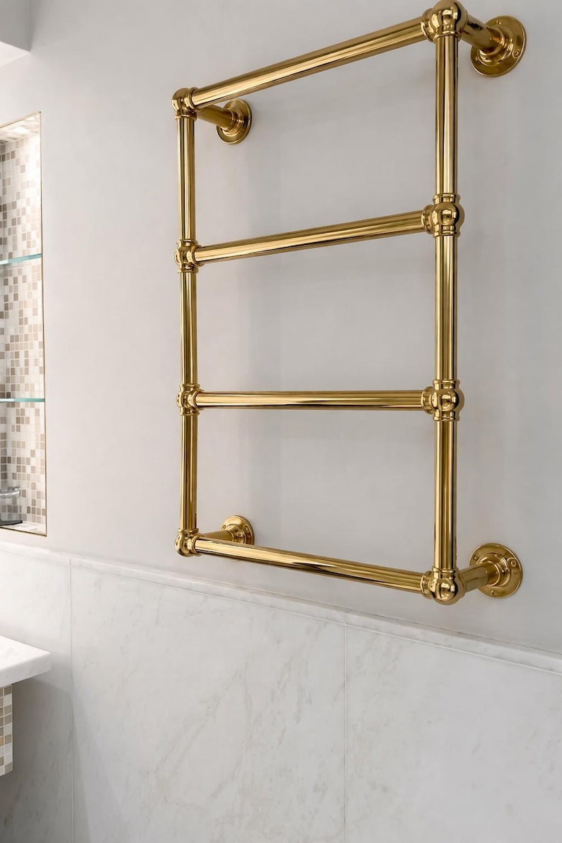 May include: A gold-colored, wall-mounted towel warmer with four horizontal bars. The design features rounded joints and circular wall mounts, creating a classic, elegant look. The warmer is installed on a white wall.