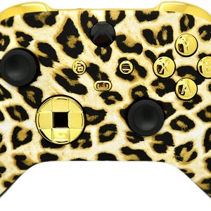 May include: A gold and black Xbox controller with a leopard print design. The controller has gold buttons and a gold D-pad.