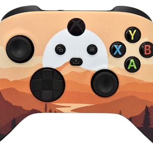 May include: A custom Xbox controller with a landscape design featuring a sunset over mountains and a river. The controller is black with orange, brown, and white accents.