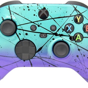 May include: A teal and purple Xbox controller with a black splatter paint design. The controller has black buttons and a black d-pad.