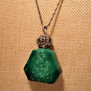 May include: A green glass bottle pendant with a silver filigree top and a silver chain. The bottle has a faceted design and is reminiscent of a vintage perfume bottle.
