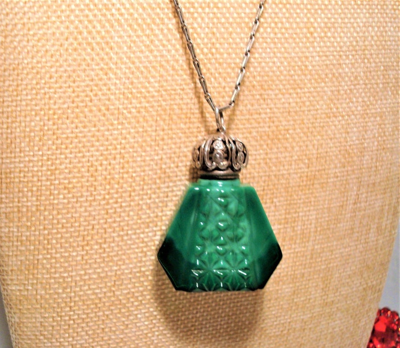 May include: A green glass bottle pendant necklace with a silver filigree stopper. The bottle has a geometric shape and a detailed design.