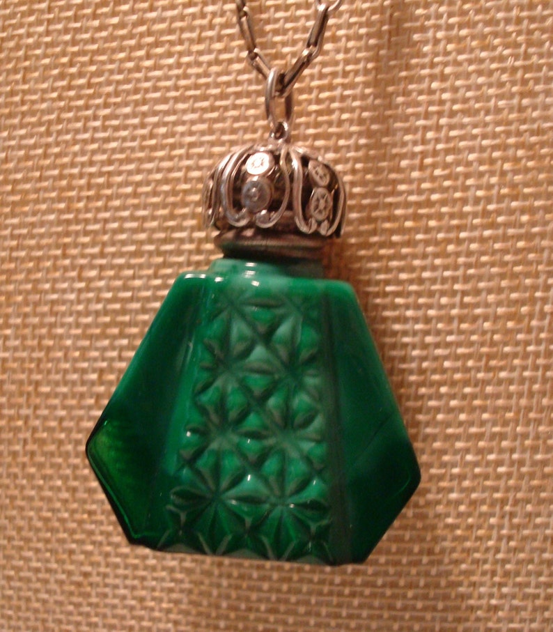 May include: A green glass bottle pendant with a silver filigree top. The bottle has a faceted design and is attached to a silver chain.