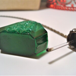 May include: A green glass bottle with a silver stopper and a dropper. The bottle has a diamond pattern on the front and is attached to a silver chain.