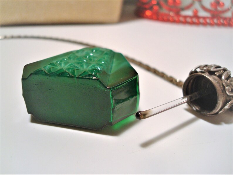 May include: A green glass bottle with a silver stopper and a dropper. The bottle has a diamond pattern on the front and is attached to a silver chain.