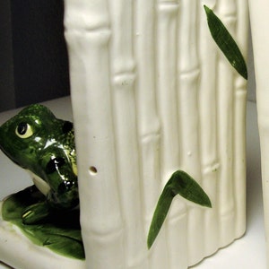 May include: A pair of white ceramic bookends shaped like bamboo stalks with green leaves and a frog on each side.