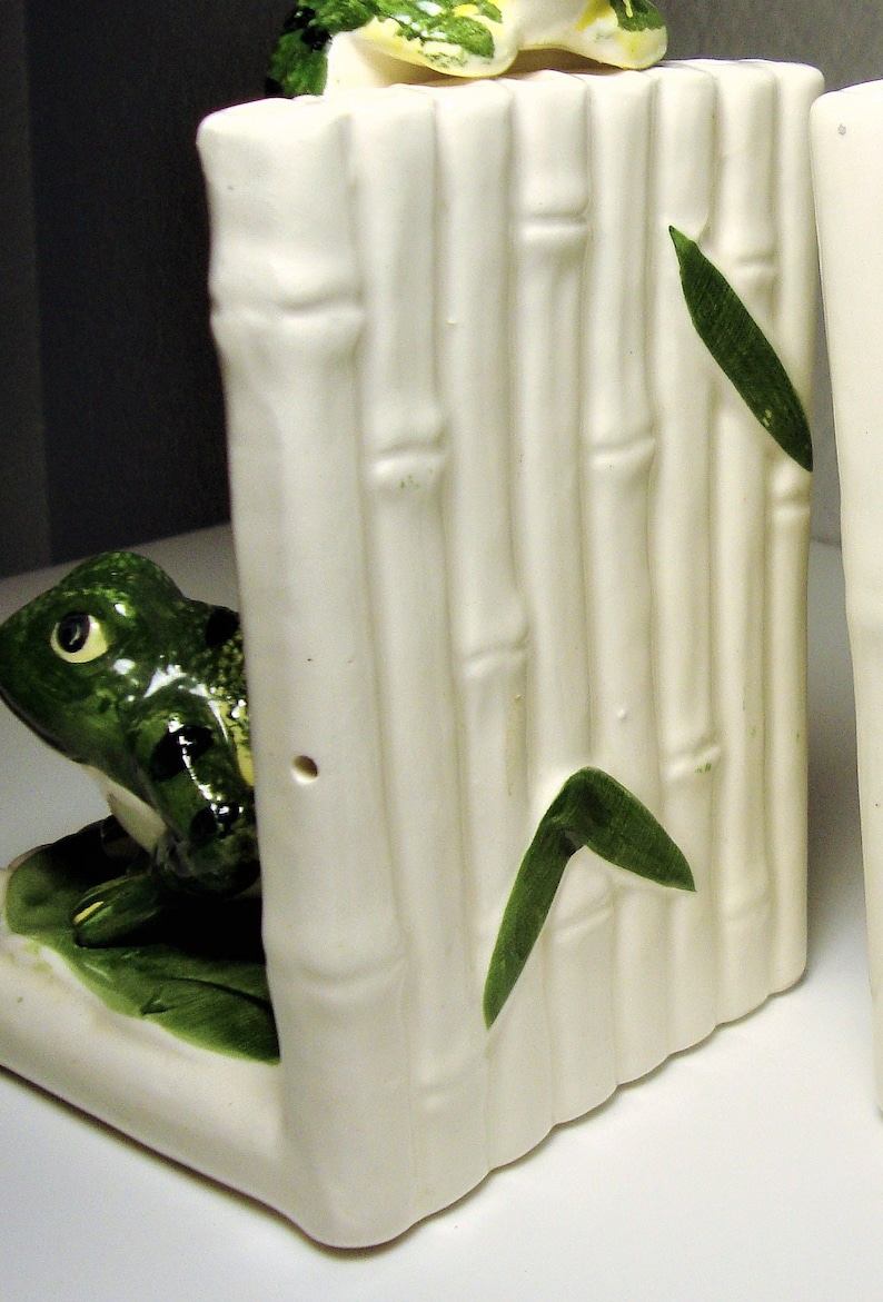 May include: A pair of white ceramic bookends shaped like bamboo stalks with green leaves and a frog on each side.