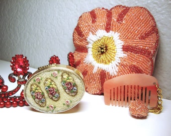 May include: A set of three vintage vanity items including a beaded floral purse, a small round compact with floral embroidery, and a pink comb with a beaded charm.