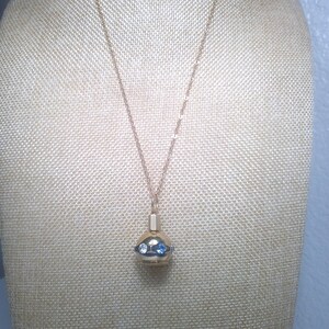 May include: A gold-toned necklace with a pendant featuring a spherical design. The pendant has blue and clear gemstones. The necklace is displayed on a beige mannequin.