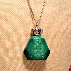 May include: A green glass bottle pendant necklace with a silver filigree top. The bottle has a geometric shape and a textured surface.