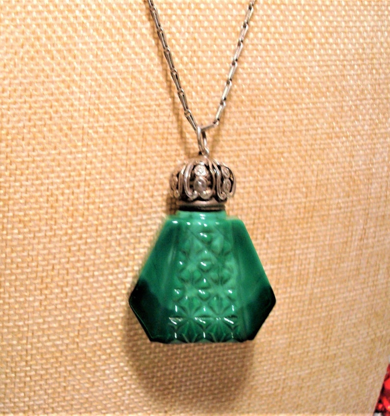 May include: A green glass bottle pendant necklace with a silver filigree top. The bottle has a geometric shape and a textured surface.