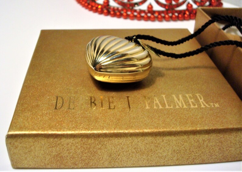 May include: A gold heart-shaped locket with a ribbed design, on a black cord necklace, in a gold box with the text "DE BEIJ PALMER TM".