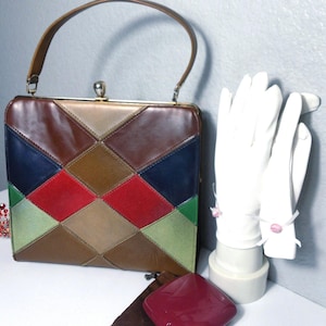 May include: A vintage handbag with a patchwork design in shades of brown, red, green, and blue. The bag has a top handle and a clasp closure. White gloves with pink bows are displayed next to the bag. A red jeweled crown is also visible.